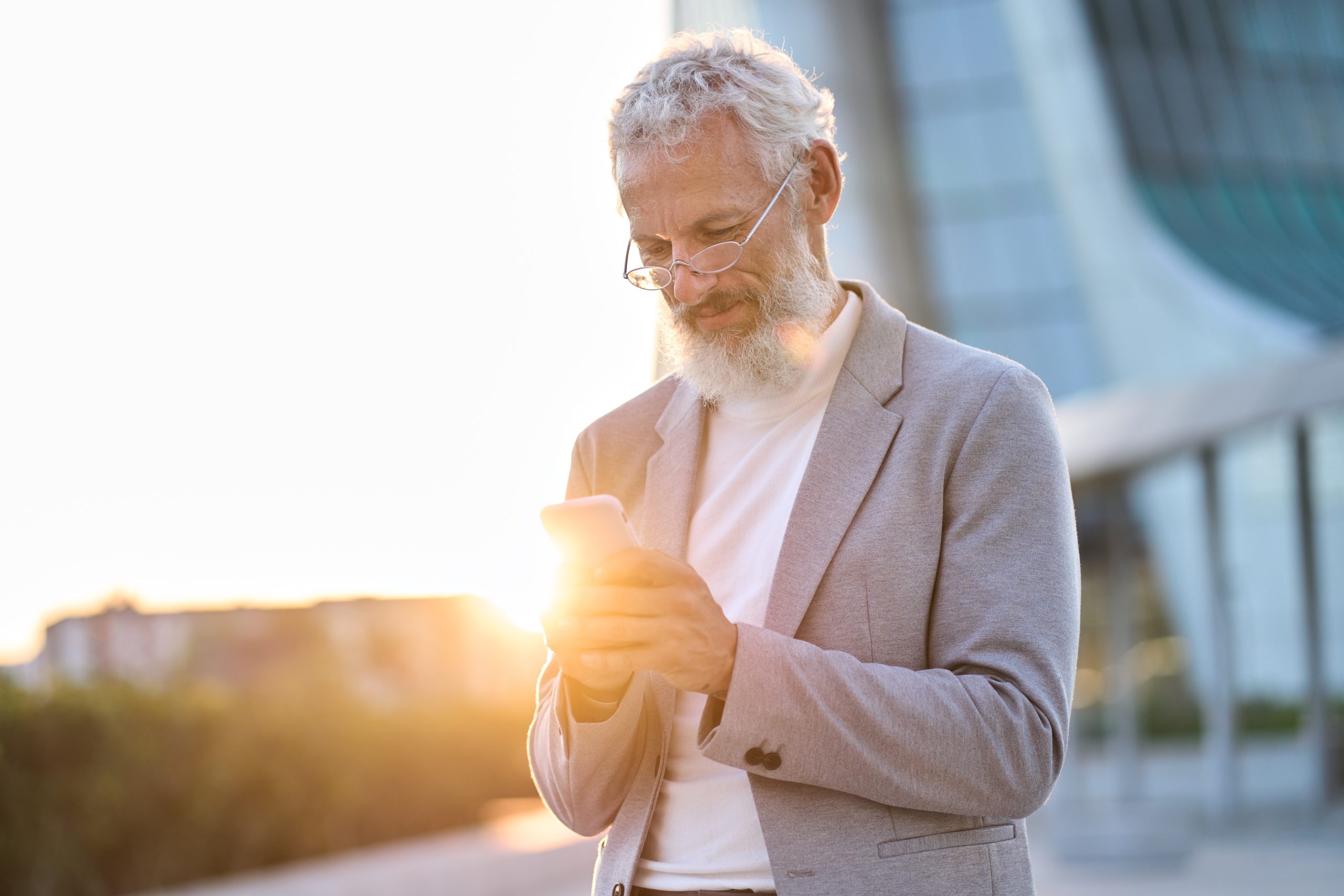 Happy older professional business man holding phone using cellphone outdoor.