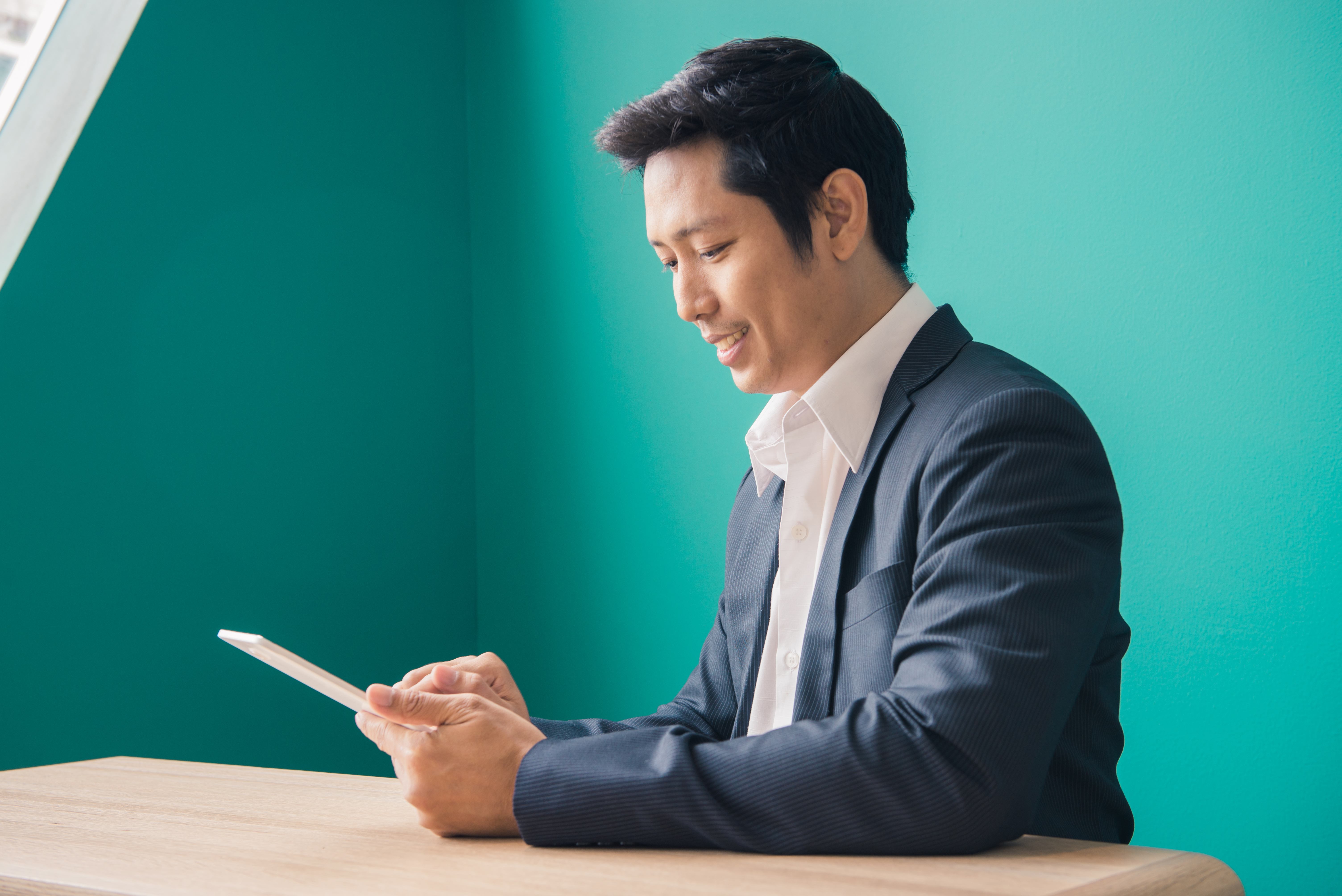 Portrait of businessman smiling and using pad at desktop against