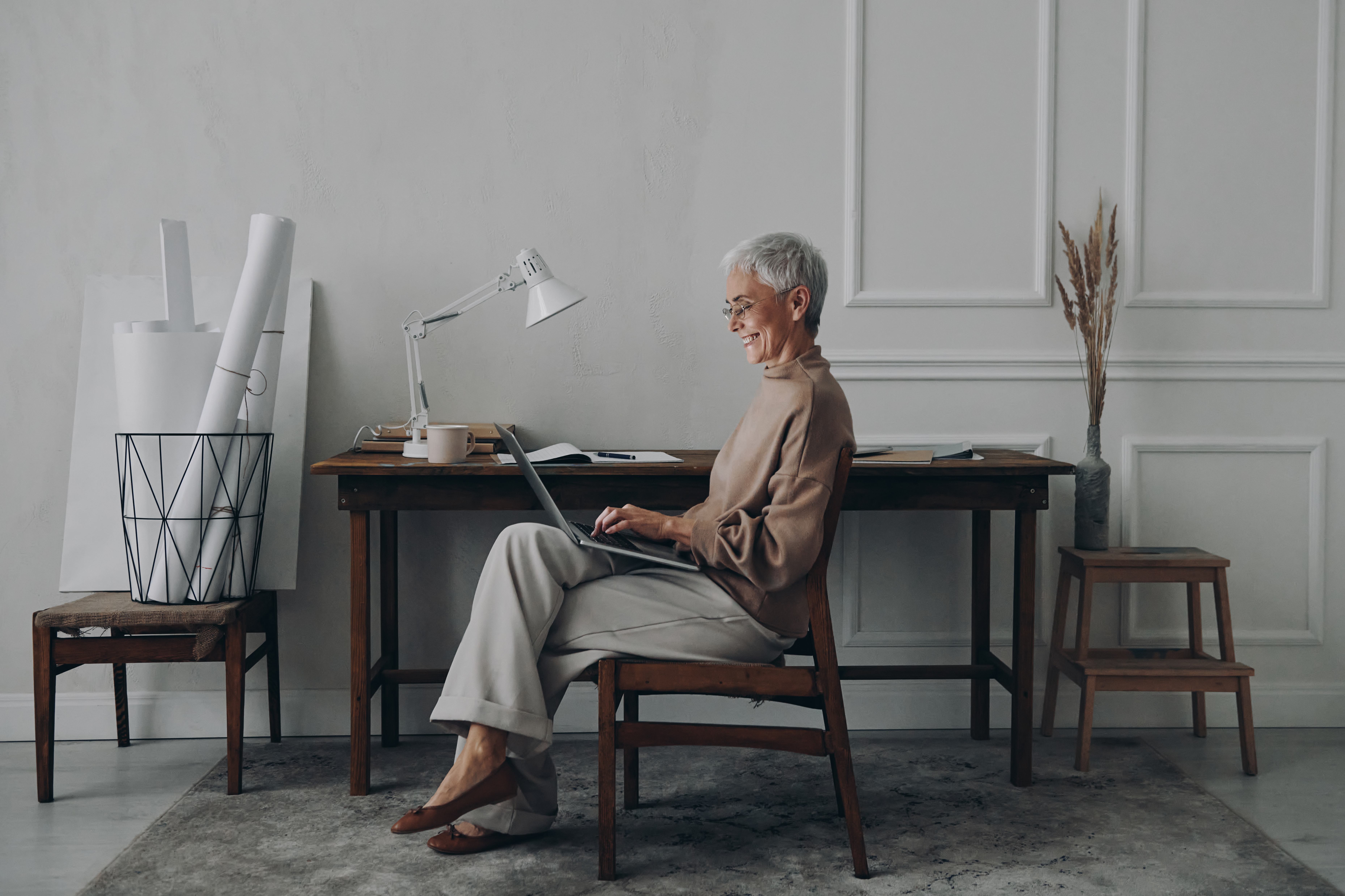 Stylish senior businesswoman using laptop and smiling while sitting at her working place